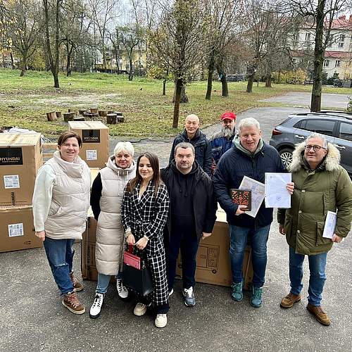 8 Personen stehen vor Kartons mit Generatoren, lächeln in die Kamera, im Hintergrund ein historisches Gebäude in der Stadt Lviv/Ukraine. lächeln